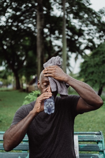 Guy outside wiping sweat off his forehead and drinking water from a plastic bottle.